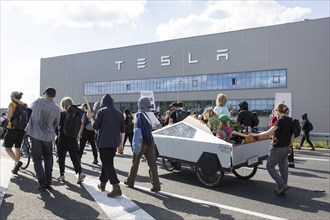 Participants with a Cybertruck cardboard model on a bicycle in front of the Tesla Gigafactory