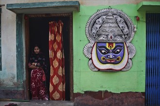 Tall mask representing a Kathakali dancer hanging on the outer wall of the house of a craftsman,