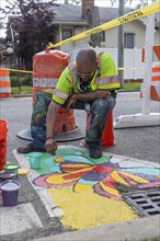 Detroit, Michigan, Artist Trae Isaac paints a design on a city street. He is part of City Walls, a