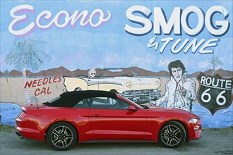 Red Ford Mustang convertible in front of mural with Elvis, Needles, California