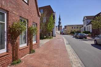 Street, house with rose bushes, buildings and St Laurentius Church in Toenning, Nordfriesland