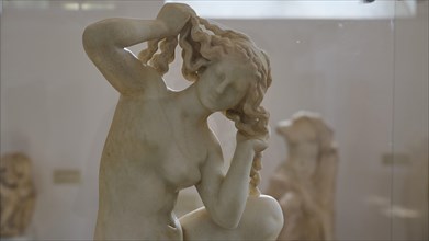 Aphrodite, crouching, close-up of a marble sculpture showing a naked woman braiding her hair,