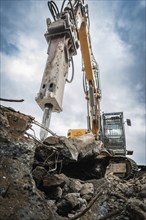 An excavator on a construction site working on a pile of rubble, large pieces of metal next to it,