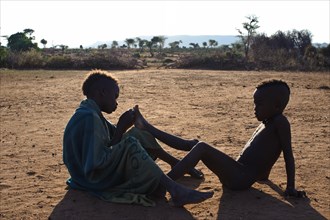 Boys from the Hamer tribe, one is removing a thorn in the foot of the other one, Omo valley,