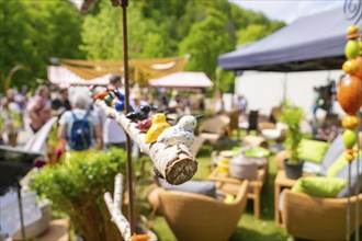An outdoor market with stalls and furniture, surrounded by green nature on a sunny day, spring,