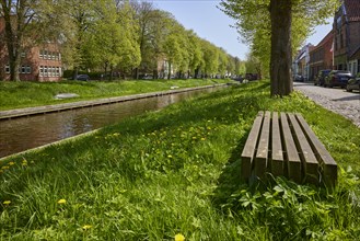 Public wooden bench between trees on the banks of the Mittelburggraben in Friedrichstadt,