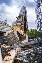An excavator's metal tongs move rubble and debris in a construction site with green background,