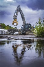 A large excavator on a construction site is reflected in a puddle under a cloudy sky, Demolition,