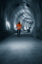 A person in a safety waistcoat walks through an illuminated, dark tunnel with a futuristic