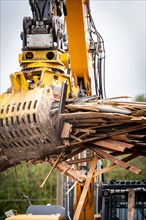 Excavator with large metal grapple crushing a pile of wood and moving on a construction site,