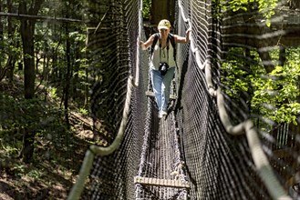 Sporty woman, tourist with camera in treetop path, suspension bridges, ropes, nets, beech forest,