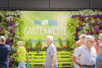 People visiting a garden fair in front of a colourful wall of flowers on a sunny day, spring,