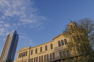 A historic building illuminated by the sunset with a modern skyscraper in the background, small