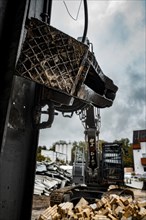 Close-up of the grab of an excavator, in the background a construction site with rubble and clouds,