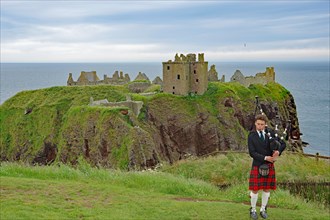 Bagpiper in front of the ruins of Dunnottar Castle, castle-like building on a cliff, Stonehaven,