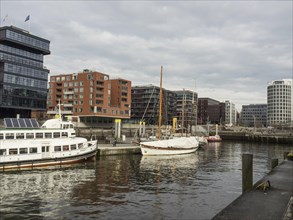Boats in the harbour, modern buildings and calm water under a cloudy sky, many ships in a harbour
