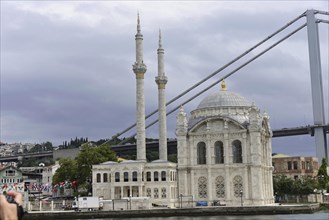 Historic mosque on a riverbank with people and bridge in the background, Istanbul, Istanbul