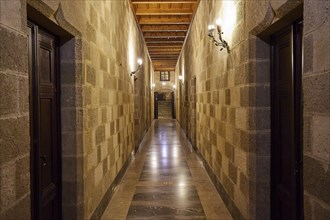 Long corridor with symmetrical stone walls and lighting, interior view, Grand Master's Palace,