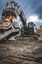 An excavator is active on a construction site, surrounded by rubble and under a dark, cloudy sky,