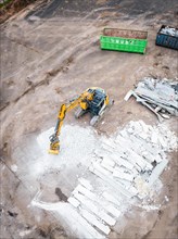 Aerial view of a construction site with a yellow excavator, demolished material and containers on