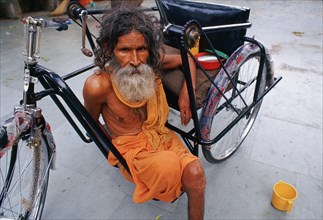 Amputee with the wheelchair he received from a charity, beggar dressed like a hindu ascetic,