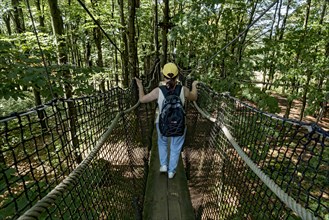 Sporty woman, tourist with rucksack in treetop path, suspension bridges, ropes, nets, beech forest,