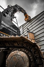 A large excavator grabs a metal structure with a mechanical grab under a cloudy sky, demolition,