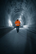 Person in safety clothing walks through an illuminated tunnel, tunnel construction Hermann