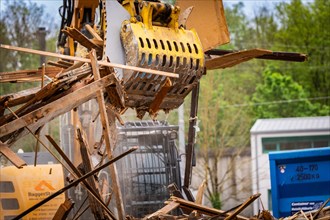 An excavator above a blue container lifts wood waste on a construction site, demolition,