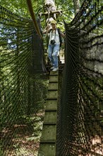 Sporty woman, tourist with camera in treetop path, suspension bridges, chicken ladder, ropes, nets,