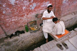 Muslim man cutting the hairs of a boy above a sewage, Peshawar, Pakistan, Asia
