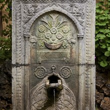 Artfully engraved stone fountain with plant motifs, water flowing out, outdoor area, Archaeological