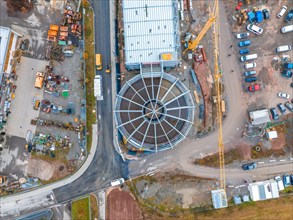 Aerial view of a large construction site with buildings, a high crane, many vehicles and roads,