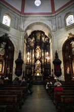 Iglesia San Nicolas de Bari, altar in a baroque church with seated people in the pews and ornate