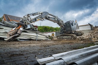 A heavy excavator lifts materials on a construction site full of rubble and pieces of metal, grey