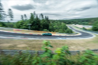 A car races around a racetrack with a bend with visible motion blur. Nuerburgring race track,