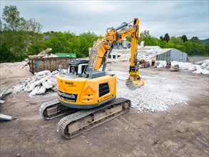 A yellow excavator on a construction site with demolished material, earth surface and containers,