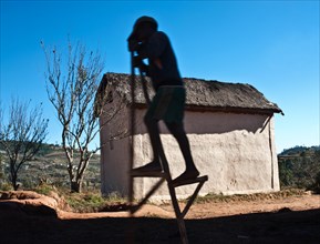 Silhouette of a boy walking on stilts, rural house in the Betsileo countryside, Madagascar, Africa