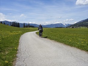 Path leads through green meadows, cyclist on the Salzkammergut cycle path, cloudy mood over