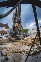 An excavator stands on a construction site, surrounded by rubble and bricks, under a cloudy sky,
