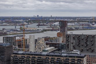 Panorama of a city with modern buildings and harbour area with cranes under a cloudy sky, view from