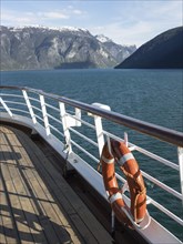 View from a ship on a calm fjord with snow-covered mountains in the background and a life belt on