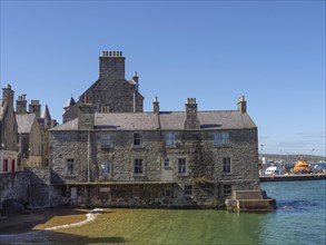 Historic building on the shore overlooking the blue-green sea and a clear sky, grey houses with