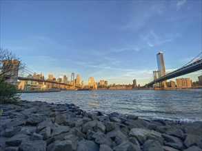 Manhattan skyline with bridges over the river at sunset seen from the shore, historic bridge in the