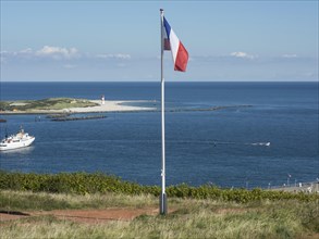 Flag waving in front of a coastal landscape with a ship in the blue sea, Heligoland, Germany,