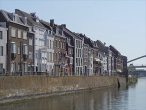 Old terraced houses along a river with a brick wall on a clear summer day, Maastricht, Netherlands