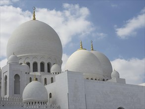 White domes of a mosque with golden jewellery under a blue sky, depicted in Islamic architecture,
