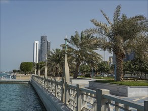 A promenade with palm trees, modern skyscrapers and clear water, Abu Dhabi, United Arab Emirates,
