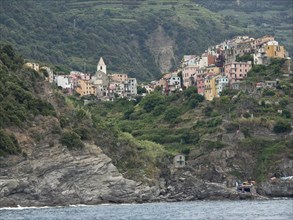 Mountain village with church and colourful houses, surrounded by green hills and rocky coast by the