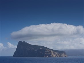 Cliff island surrounded by the blue sea with a large cloud above in a calm, clear atmosphere, palma